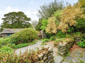 Ein gepflasterter Weg schlängelt sich durch einen Garten mit verschiedenen Pflanzen und einer Steinmauer.