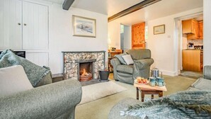 A living room with a stone fireplace, a grey armchair, and a sofa. - 2 Bed in Keswick (oc-sz302) (Rosthwaite)