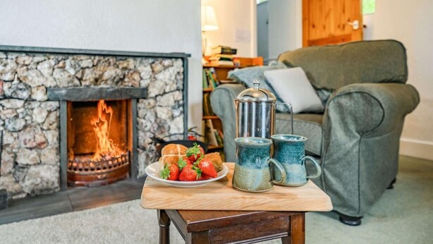 A cozy living room with a stone fireplace, a green sofa, and a table with a plate of strawberries and two mugs. - 2 Bed in Keswick (oc-sz302) (Rosthwaite)