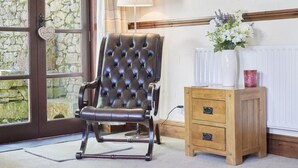 A room with a leather armchair, a wooden cabinet, a lamp, and a window with a stone wall view. - 1 Bed in Holmrook (oc-sz471) (Irton with Santon)