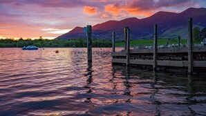 Un lago tranquilo con un muelle de madera, montañas al fondo y un bote en el agua.