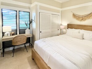 Ein Schlafzimmer mit Bett, Schreibtisch, Stuhl, Lampe und einem Fenster mit Jalousien.