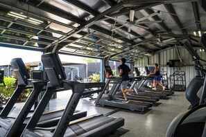 Ein Fitnessstudio mit mehreren Laufbändern, Trainingsgeräten und einer Decke mit Oberlichtern.