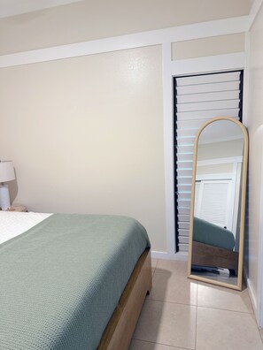 A bedroom with a bed, a mirror, a nightstand, and a door with blinds. - Luxe Kauai 1BR Retreat | A/C & Beach Access (Koloa)