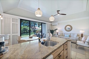 A modern kitchen with a granite countertop, stainless steel sink, and a dining area with wicker chairs. - Luxe Kauai 1BR Retreat | A/C & Beach Access (Koloa)