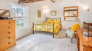 Ein Schlafzimmer mit Bett, Kommode, Fenster und Holzbalken an der Decke.