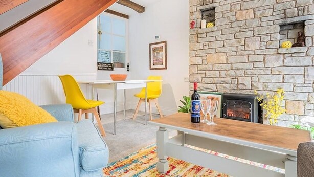 Ein gemütliches Wohnzimmer mit Kamin aus Stein, einem Essbereich mit gelben Stühlen und einem blauen Sofa.