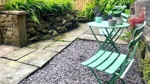 Eine Terrasse mit einer Steinmauer, einem Holenzaun und einem Tisch mit Stühlen.