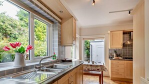 A kitchen with a large window, a sink, and a table with a tablecloth. - 3 Bed in Keswick (oc-sz249) (Keswick)
