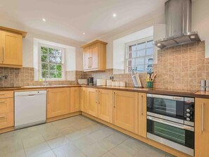 A kitchen with wooden cabinets, a dishwasher, a double oven, and a window. - 4 Bed in Penrith (oc-sz383) (Skirwith)