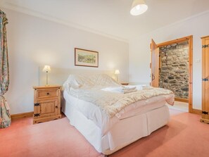 A bedroom with a bed, bedside tables, a lamp, a framed picture, and a stone wall. - 4 Bed in Penrith (oc-sz383) (Skirwith)