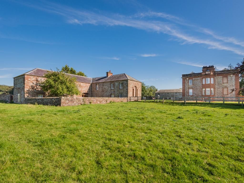 A large stone building with multiple windows and a grassy field in front.