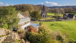 Een stenen kerk met een puntige toren, een stenen muur en een grasveld.