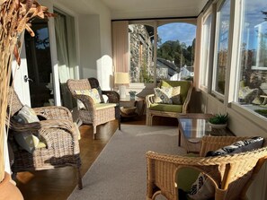 Ein gemütliches Zimmer mit Korbmöbeln, einem kleinen Tisch und Blick auf ein Steinhaus durch ein Fenster.