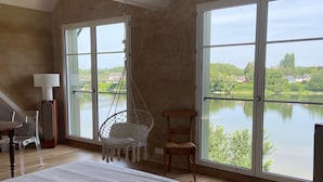 Ein Schlafzimmer mit einem großen Bett, einem Hängekorbsessel, einem Holzstuhl und Seeblick durch große Fenster.