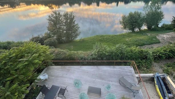 Ein Seeufer mit Terrassenausstattung, einem Boot und Blick auf den See sowie die umliegenden Bäume.