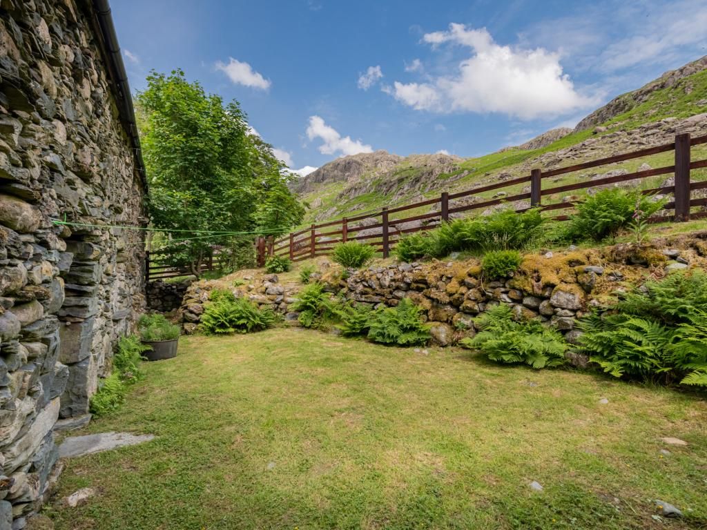Un mur de pierres, une clôture en bois et une zone herbeuse parsemée de fougères.
