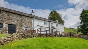 A stone building with a white exterior, a wooden fence, and a grassy yard. - 3 Bed in Broughton-in-furness (oc-sz107) (Eskdale)