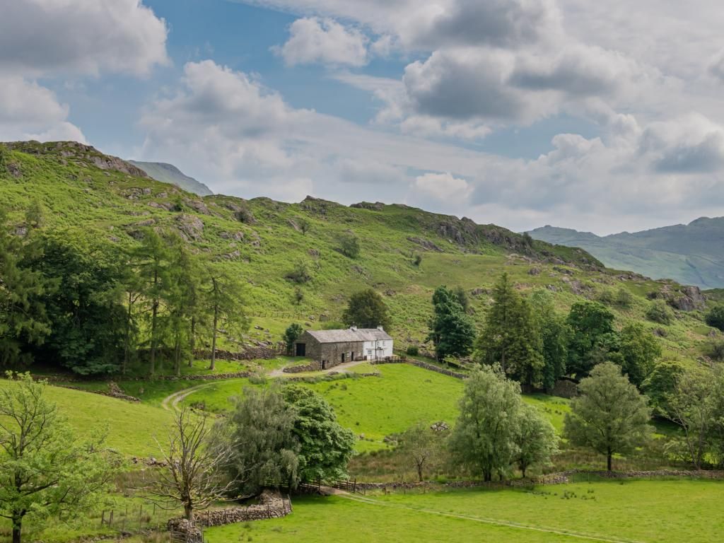 A rural landscape with a stone house surrounded by green fields and trees.