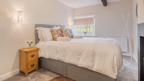 Quarto com cama, mesa de cabeceira, luminária, janela e vista para o verde lá fora.