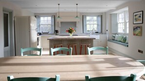 A modern kitchen with a central island, pendant lighting, and a dining area with a wooden table and chairs. - 4 Bed in Penrith (oc-sz264) (Askham)