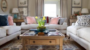 A living room with two sofas, a coffee table with books and a vase of flowers, a patterned rug, and framed pictures on the walls. - 4 Bed in Penrith (oc-sz264) (Askham)