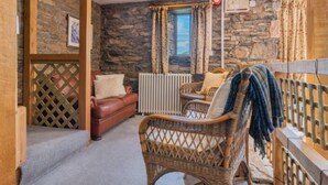Een gezellige kamer met stenen muren, een bruine leren bank, rieten stoelen en uitzicht door een raam met gordijnen.