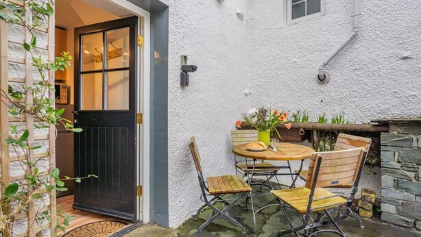 Un petit espace extérieur aménagé avec une table et des chaises, un pot de fleurs et une porte donnant sur une pièce.