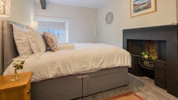 A bedroom with a bed, bedside table, lamp, fireplace, and window. - 2 Bed in Keswick (oc-sz199) (Underskiddaw)