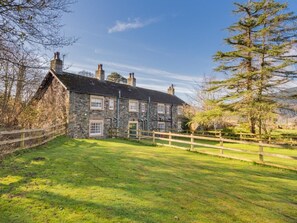 Ein Steinhaus mit umzäuntem Garten und einem großen Baum.