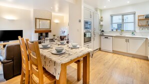 Una cucina moderna con mobili bianchi, un tavolo da pranzo per quattro persone e una televisione a schermo piatto nella zona soggiorno.