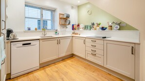 Una cucina moderna con lavastoviglie, mobili in legno, una finestra con persiane e una parete verde decorativa.