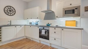 Ett modernt kök med vita köksskåp, en mikrovågsugn i rostfritt stål, en blå vattenkokare och en klocka på väggen.