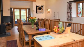 A dining area with wooden furniture, a table with a vase of flowers, a fruit bowl, and a wooden railing. - 2 Bed in Penrith (oc-sz470) (Patterdale)