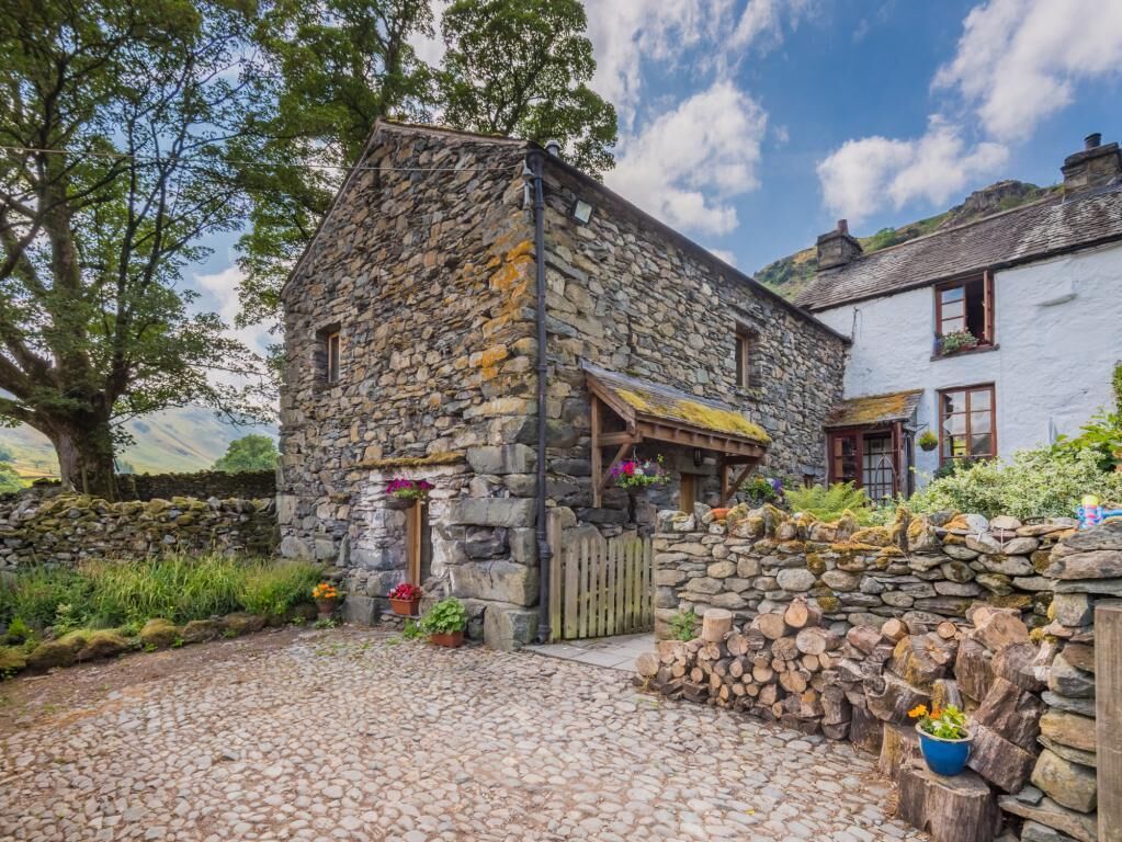 A stone building with a wooden door, a stone wall, and a garden with potted plants.