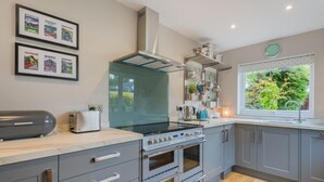 A modern kitchen with grey cabinets, a built-in oven, a stove, and a window with a view of greenery. - 3 Bed in Keswick (oc-sz029) (Keswick)