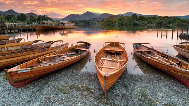 Wooden boats docked at a lakeside pier with a mountain backdrop. - 3 Bed in Keswick (oc-sz029) (Keswick)