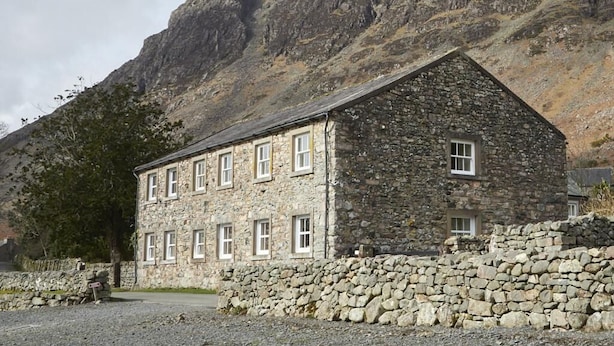 A stone building with multiple windows, a stone wall in front, and a mountainous backdrop. - 2 Bed in Wasdale Head (oc-sz551) (Wasdale)