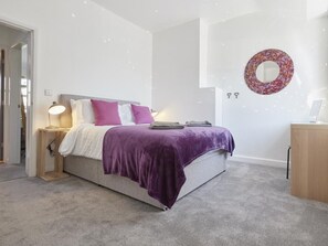 Quarto com cama, mesas de cabeceira, luminária, espelho fixado na parede e um pequeno armário de madeira.