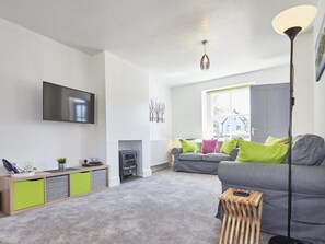 Ein modernes Wohnzimmer mit einem grauen Sofa, einem Holztisch, einem an der Wand montierten Fernseher und einer Stehlampe.