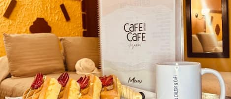 A hotel room with a cozy seating area featuring a sofa and a table with a plate of pastries and a menu.