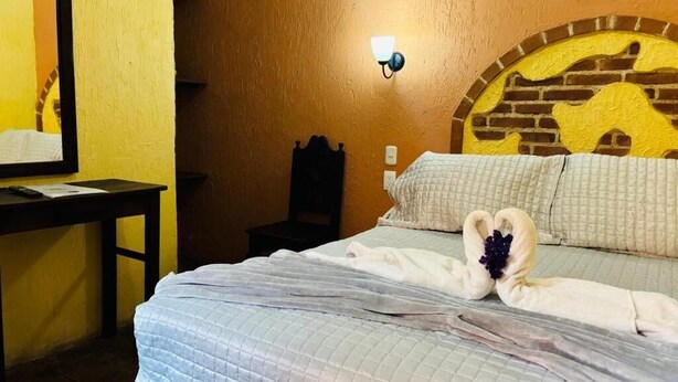 Una habitación de hotel con cama, mesita de noche, lámpara de pared y una decoración en la pared.