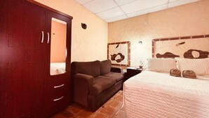 A bedroom with a bed, a wardrobe, a sofa, and a ceiling fan.