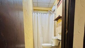 Baño estrecho con inodoro, lavamanos y cortina de ducha.