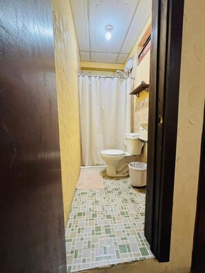 Baño estrecho con inodoro, lavamanos y cortina de ducha.
