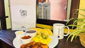 A breakfast plate with eggs, beans, and plantains, a menu, and a coffee cup on a wooden table.