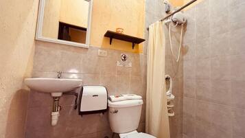 A bathroom with a sink, toilet, mirror, shower, and a trash bin.