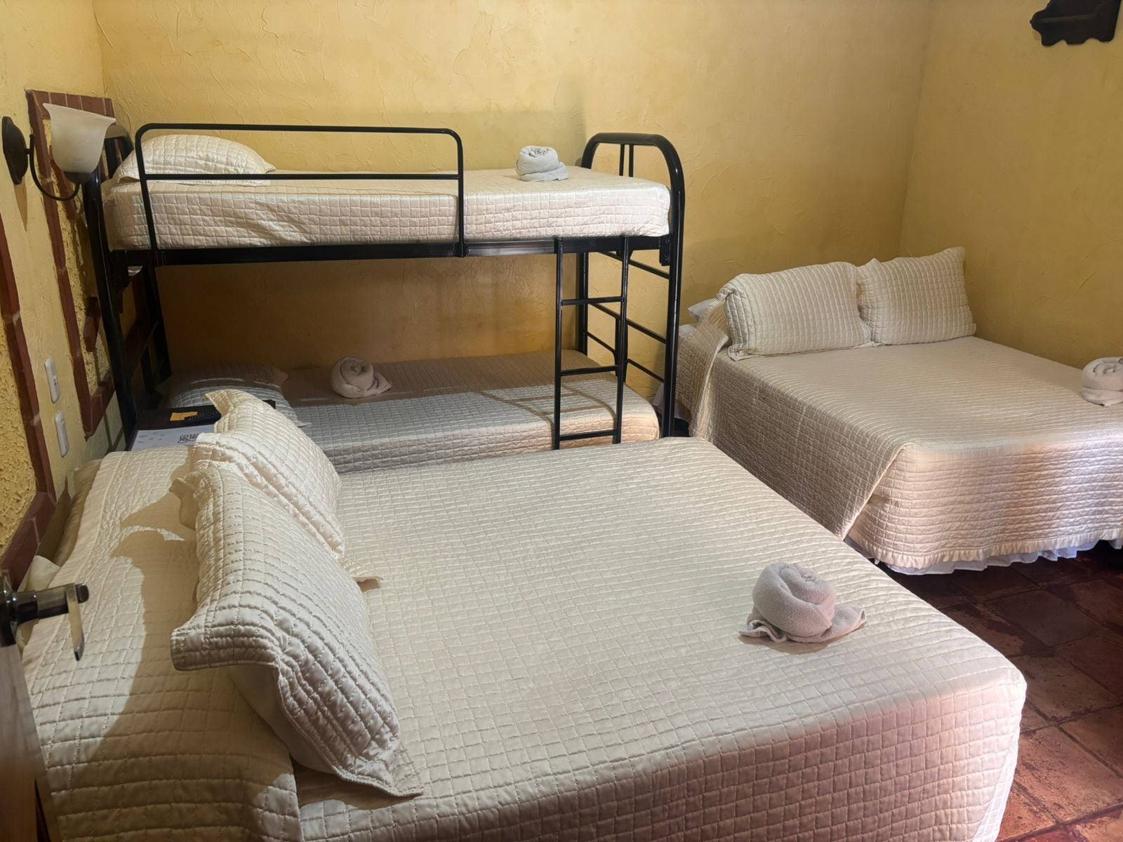 A dormitory room with bunk beds and two single beds, each with a quilted mattress and pillows.