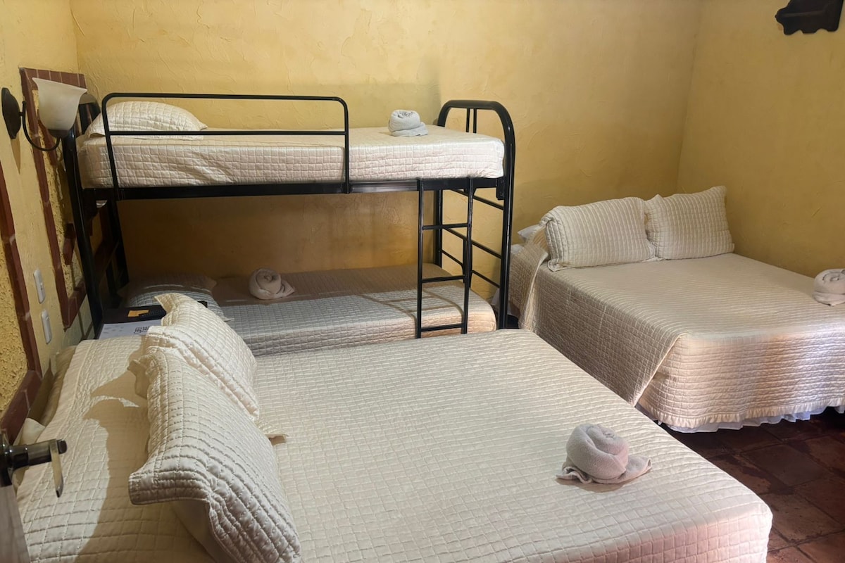 A dormitory room with bunk beds and two single beds, each with a quilted mattress and pillows.