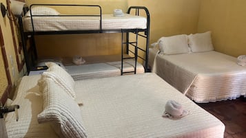 A dormitory room with bunk beds and two single beds, each with a quilted mattress and pillows.